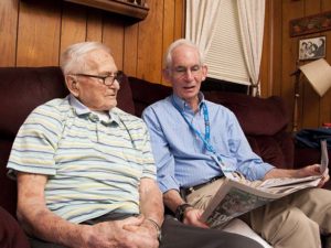 Care Dimensions Veteran-to-Veteran volunteer with hospice patient reviewing sports section of newspaper